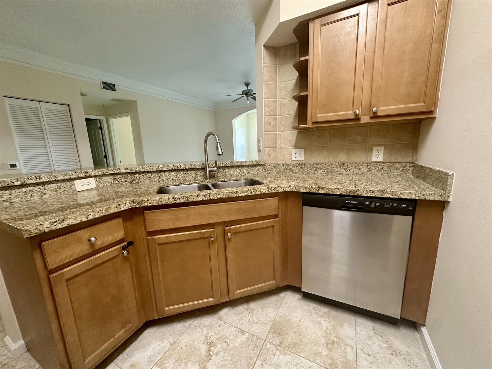 A kitchen features light wood cabinets, granite countertops, a stainless steel dishwasher, and tile flooring — 9901 Baywinds # 3105, West Palm Beach FL 33411, WEST PALM BEACH, FL