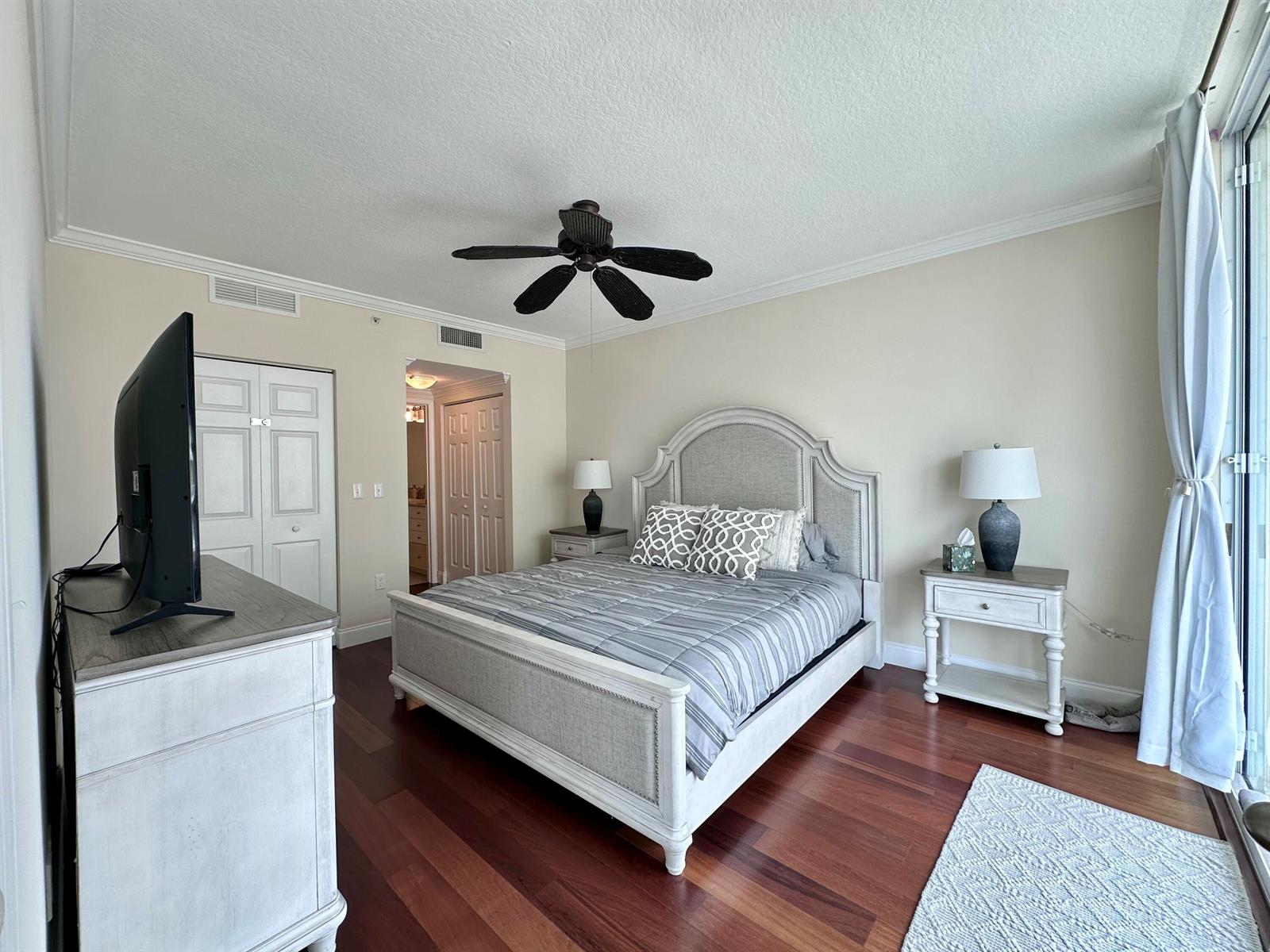 A bedroom features a bed with a gray upholstered headboard, wooden floors, and a ceiling fan — 700 E Boynton Beach Boulevard # 1203, Boynton Beach FL 33435, BOYNTON BEACH, FL