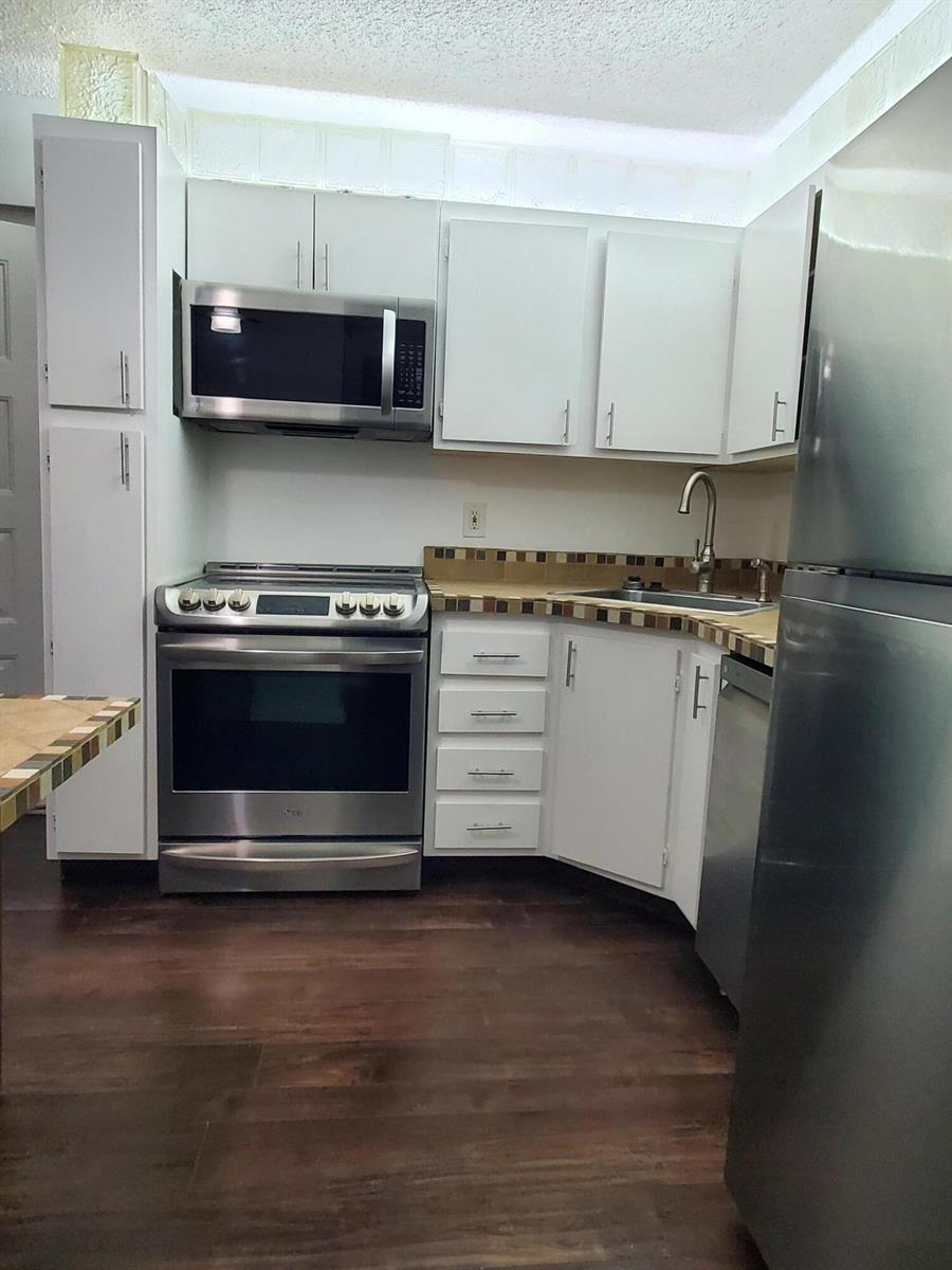 A kitchen features white cabinets, stainless steel appliances, a tiled backsplash, and dark wood flooring — 603 Sea Pine Way # B2, FL 33415, FL