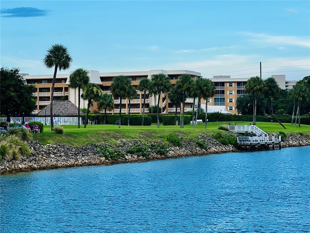 A multi-story apartment building sits behind a grassy lawn, palm trees, and a wooden dock — 304 GOLFVIEW ROAD UNIT PH7, NORTH PALM BEACH, FL