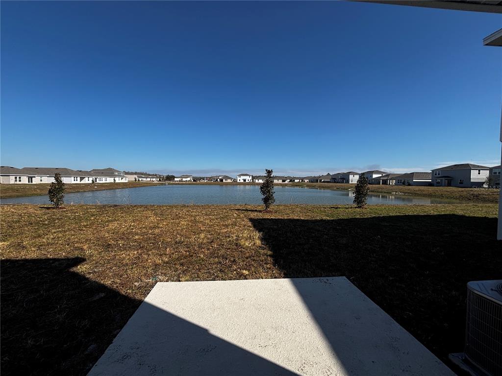 A concrete patio overlooks a retention pond surrounded by suburban houses under a clear sky — 4763 GUINEP LANE, KISSIMMEE, FL