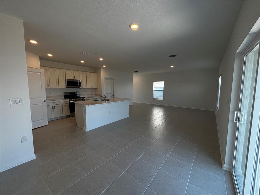 An open-concept kitchen and living area featuring white cabinets, a central island, and tile flooring — 4763 GUINEP LANE, KISSIMMEE, FL