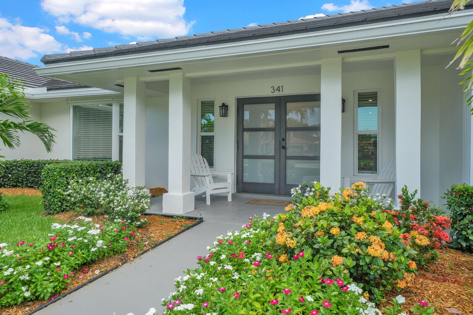 A white house exterior features a gray double front door, white columns, and colorful landscaping — 341 Glenbrook Drive, Atlantis FL 33462, ATLANTIS, FL