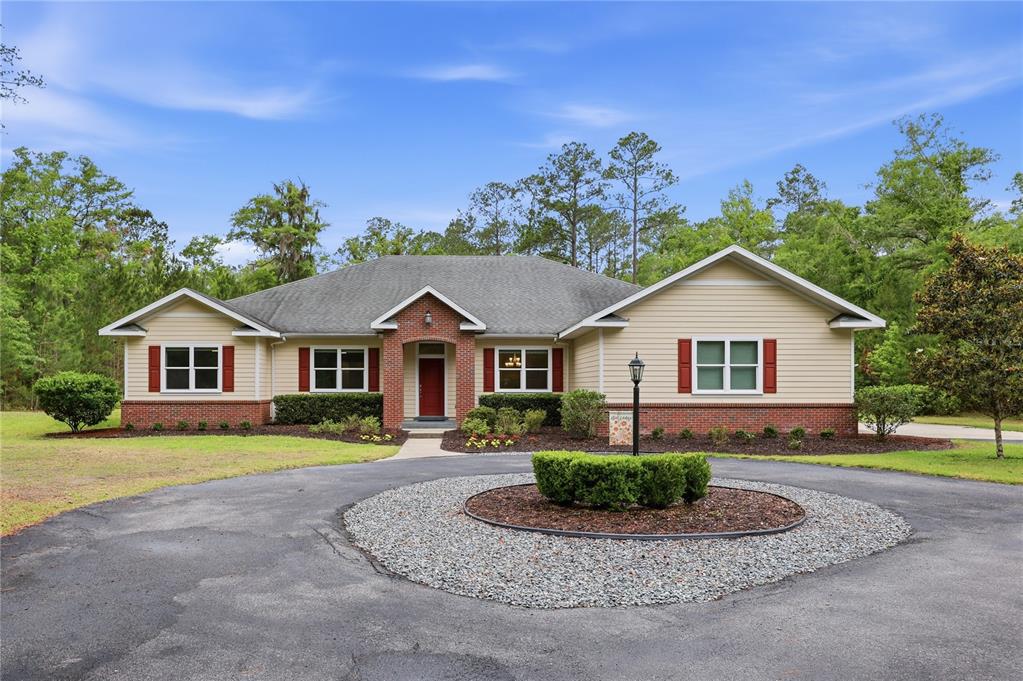 A paved driveway leads through an open black metal gate toward a single-story brick house — 9208 NW 64TH TERRACE, GAINESVILLE, FL