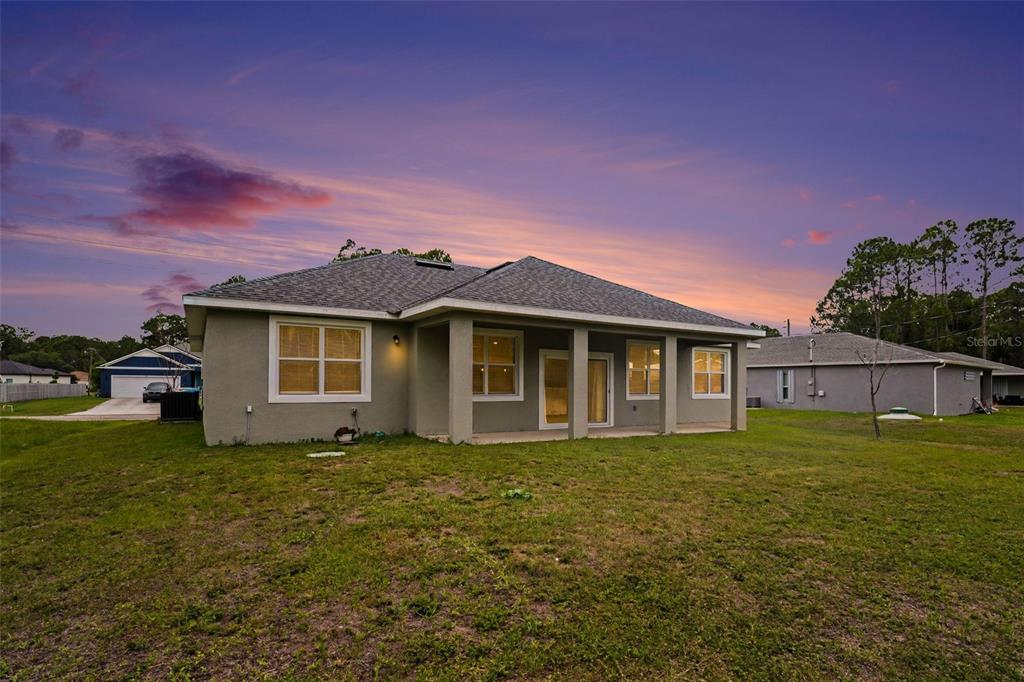 The rear exterior of a single-story house features a covered patio and a grassy yard — 333 KRASSNER DRIVE NW, PALM BAY, FL