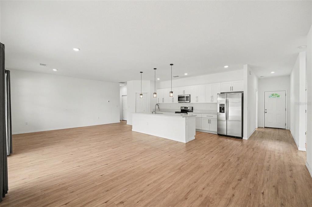 An open-concept kitchen and living area features white cabinetry, stainless steel appliances, and wood flooring — 333 KRASSNER DRIVE NW, PALM BAY, FL
