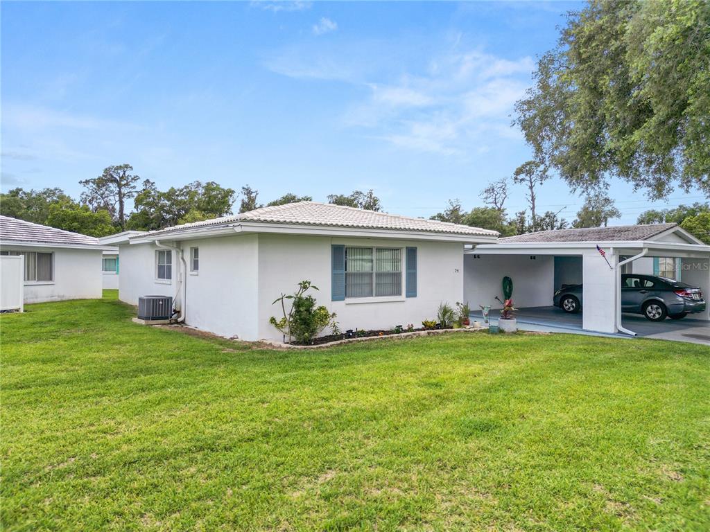 A white single-story house with a carport and a grassy lawn under a blue sky — 711 BARBER CIRCLE UNIT 711, LAKELAND, FL