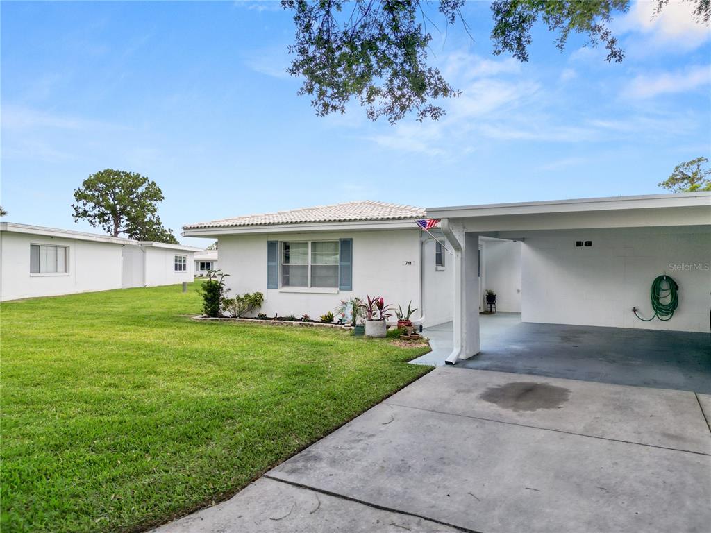 A white single-story house features a concrete driveway and an attached carport — 711 BARBER CIRCLE UNIT 711, LAKELAND, FL