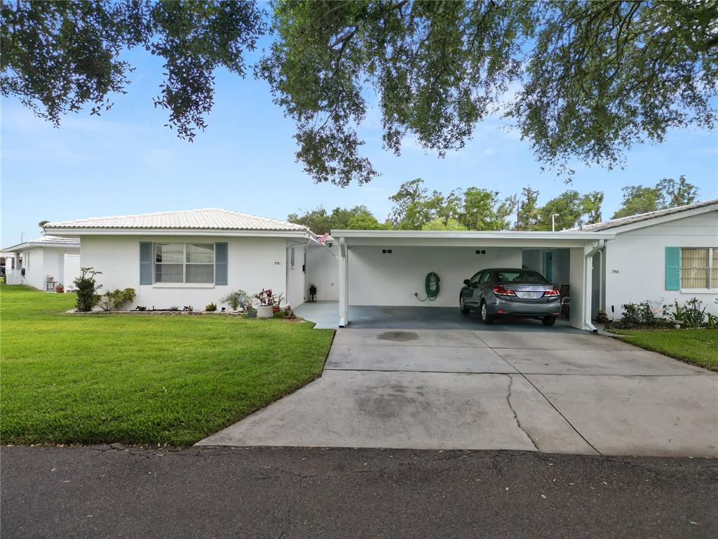 A white single-story house features a concrete driveway, a carport, and a green lawn — 711 BARBER CIRCLE UNIT 711, LAKELAND, FL