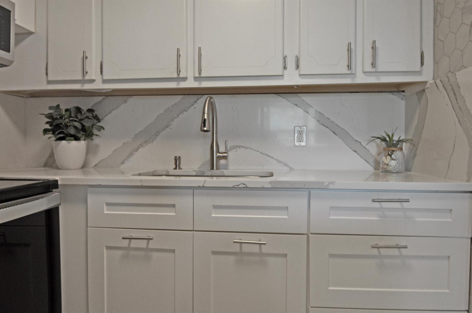 A kitchen features white cabinets, a marble-patterned backsplash, and a stainless steel sink faucet — 238 Chatham L, West Palm Beach FL 33417, WEST PALM BEACH, FL