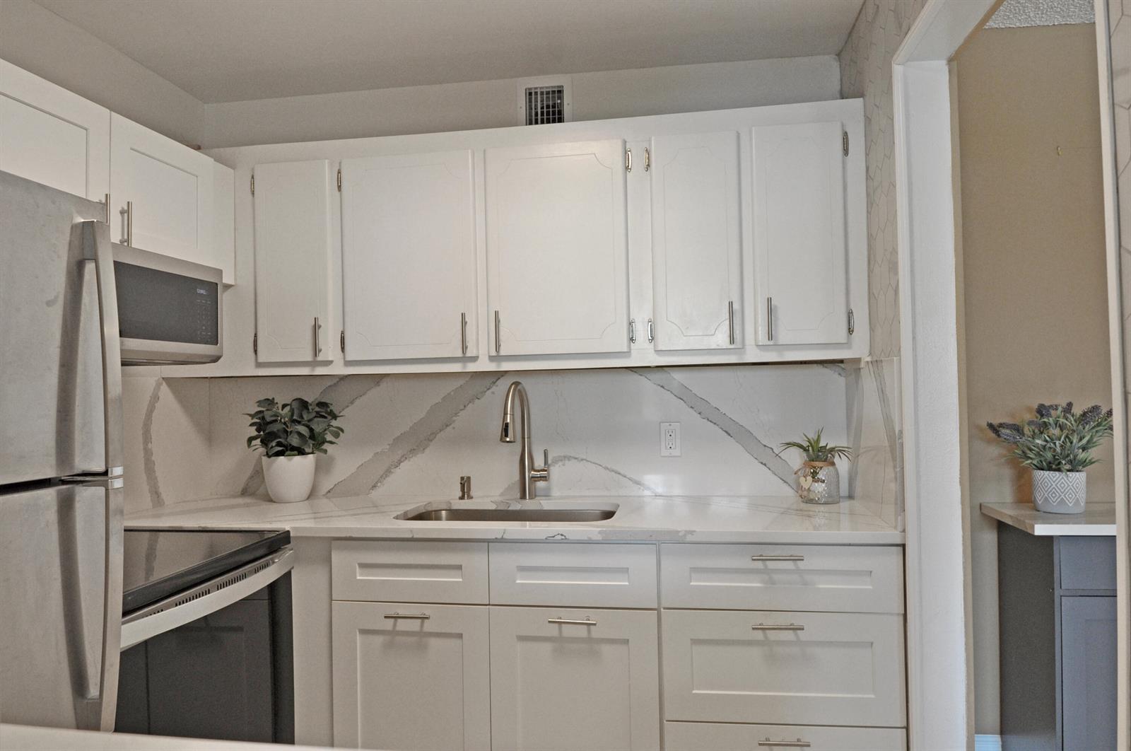 A kitchen features white cabinets, stainless steel appliances, and a marble-patterned countertop and backsplash — 238 Chatham L, West Palm Beach FL 33417, WEST PALM BEACH, FL