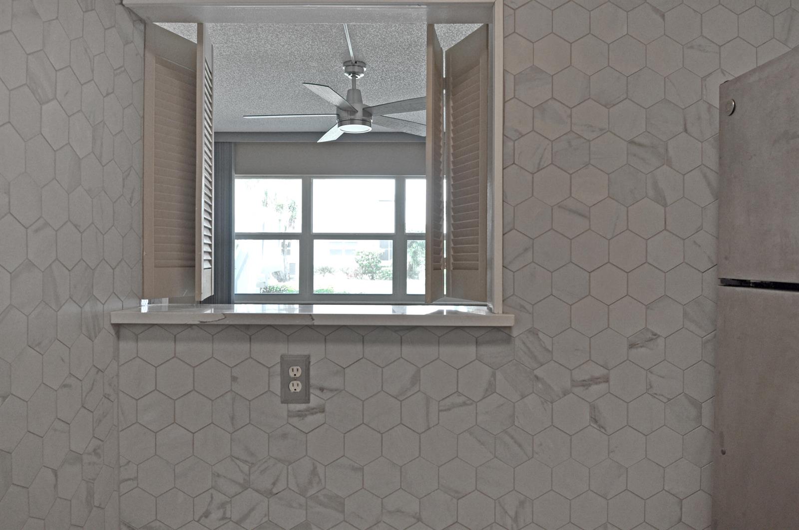 A kitchen pass-through window features white marble-look hexagonal tile walls and wooden shutters — 238 Chatham L, West Palm Beach FL 33417, WEST PALM BEACH, FL