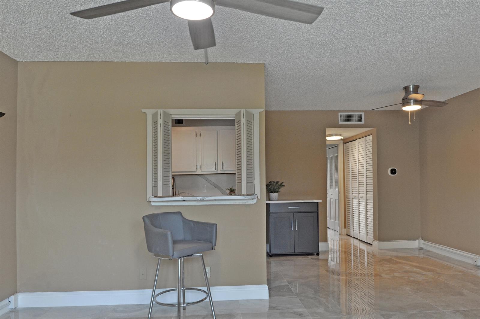 A living area features a kitchen pass-through window, a gray bar stool, and tile flooring — 238 Chatham L, West Palm Beach FL 33417, WEST PALM BEACH, FL