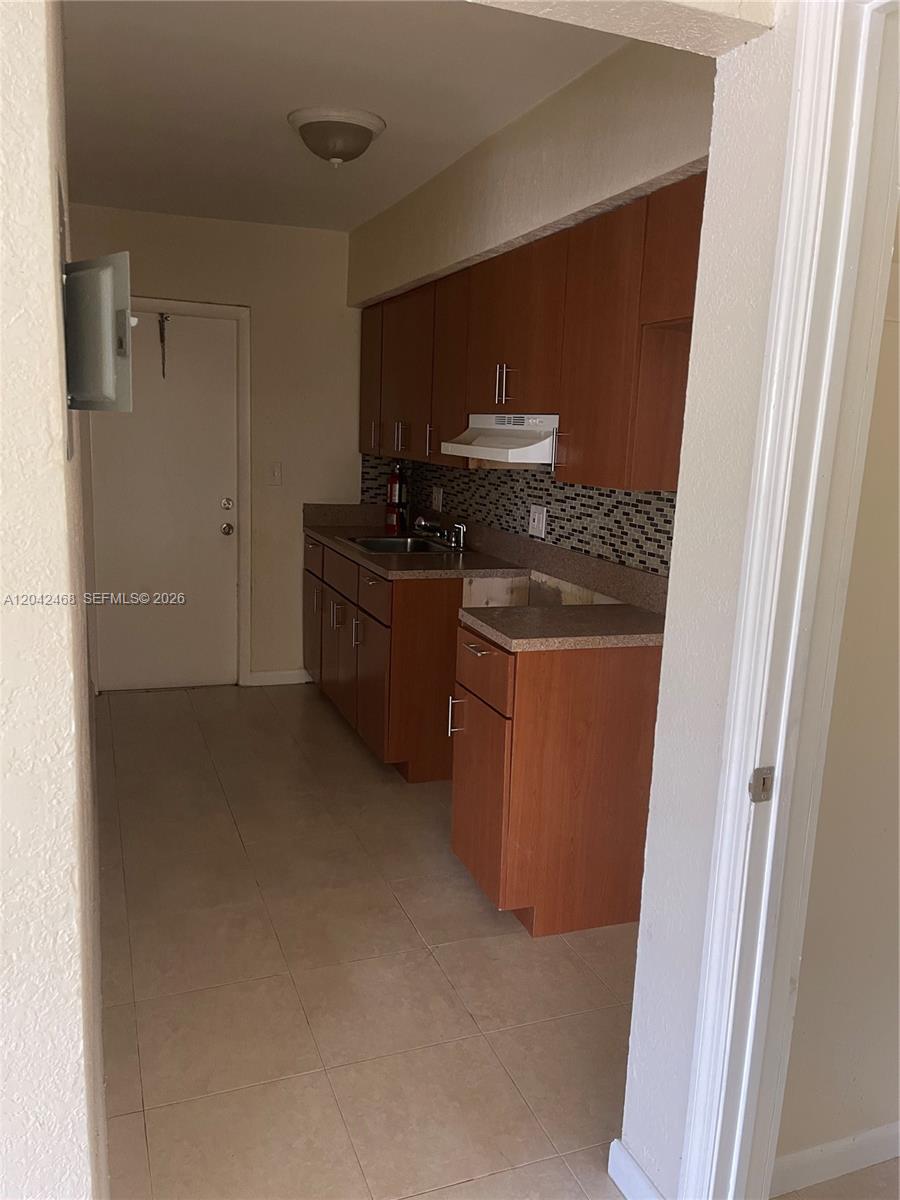 This kitchen features wood cabinets, a tiled backsplash, and light-colored floor tiles — 16041 NE 18th Pl # 1, North Miami Beach FL 33162, NORTH MIAMI BEACH, FL