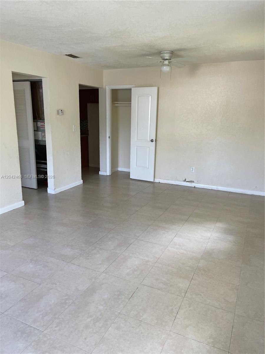 An empty room features beige walls, light-colored tile flooring, a ceiling fan, and two doorways — 16041 NE 18th Pl # 1, North Miami Beach FL 33162, NORTH MIAMI BEACH, FL