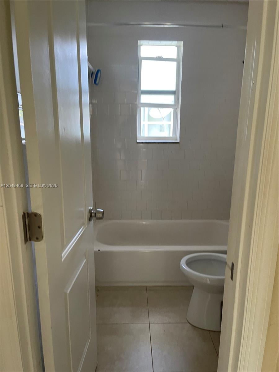 A bathroom features a white bathtub, tiled walls, a window, and a toilet — 16041 NE 18th Pl # 1, North Miami Beach FL 33162, NORTH MIAMI BEACH, FL