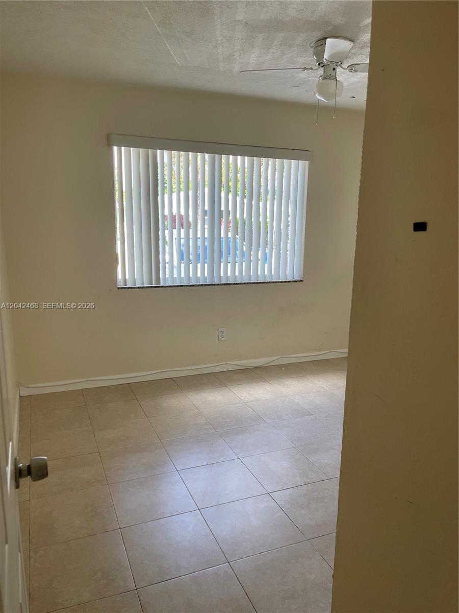 This room features light-colored tile flooring, beige walls, and a window with vertical blinds — 16041 NE 18th Pl # 1, North Miami Beach FL 33162, NORTH MIAMI BEACH, FL