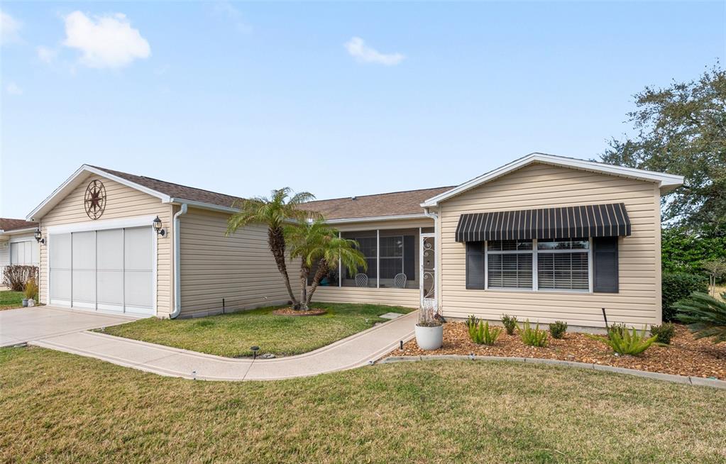 A single-story house with beige siding, a garage, a screened porch, and a striped awning — 2001 CIPRIANO PLACE, THE VILLAGES, FL