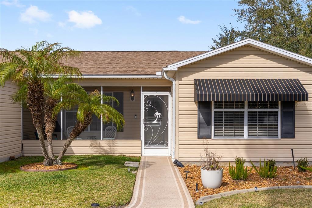 A beige house exterior features a screened-in porch, a palm tree, and a striped awning — 2001 CIPRIANO PLACE, THE VILLAGES, FL