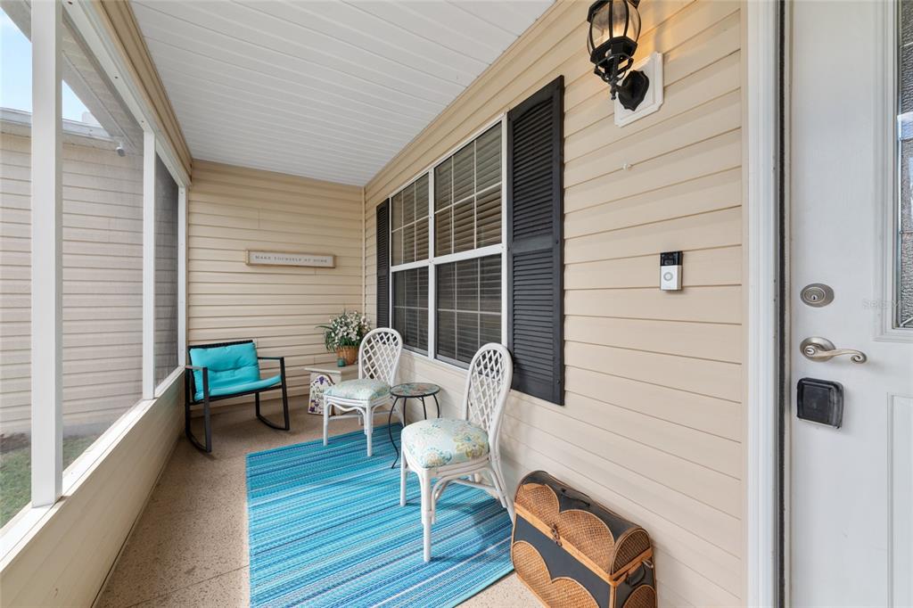 A screened-in porch features beige siding, a blue striped rug, and white patio furniture — 2001 CIPRIANO PLACE, THE VILLAGES, FL
