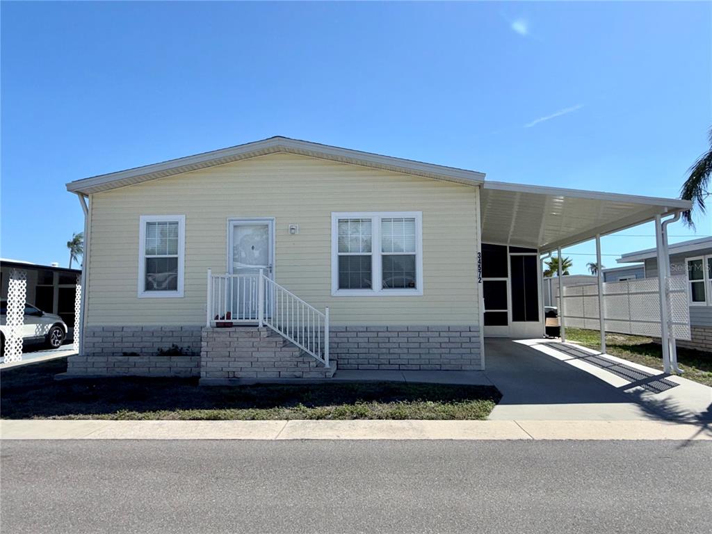 A light yellow manufactured home features a front porch, a carport, and brick skirting — 34572 GARDENIA DRIVE N, PINELLAS PARK, FL