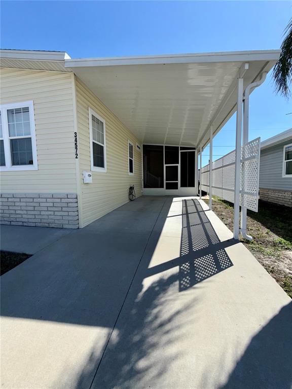 A pale yellow manufactured home features a concrete driveway and a covered carport — 34572 GARDENIA DRIVE N, PINELLAS PARK, FL
