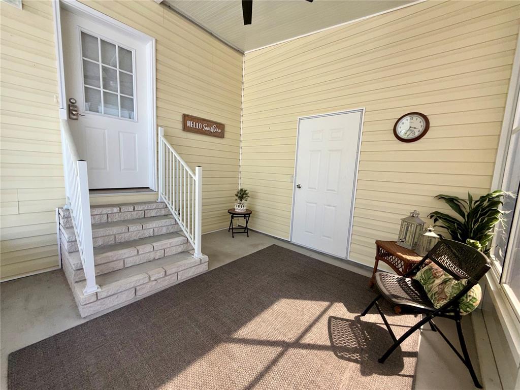 A covered porch features light yellow siding, a set of stone steps, and a brown rug — 34572 GARDENIA DRIVE N, PINELLAS PARK, FL