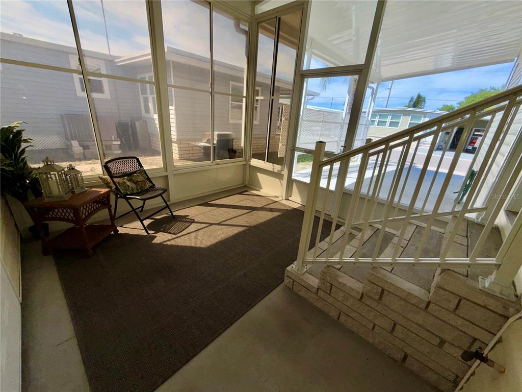 A screened-in porch features a brown area rug, a chair, and stairs with a railing — 34572 GARDENIA DRIVE N, PINELLAS PARK, FL