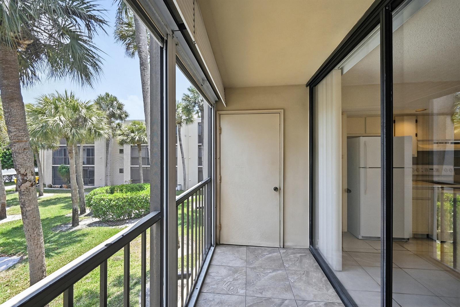 A screened-in balcony with tiled flooring overlooks a grassy courtyard with palm trees — 5370 Las Verdes Circle # 219, Delray Beach FL 33484, DELRAY BEACH, FL