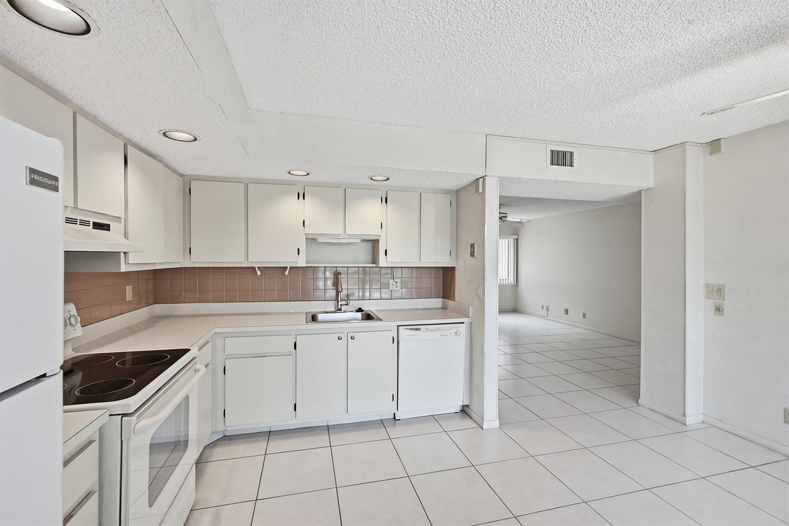 A kitchen with white cabinets, tile flooring, and a tiled backsplash opens to a living area — 5370 Las Verdes Circle # 219, Delray Beach FL 33484, DELRAY BEACH, FL