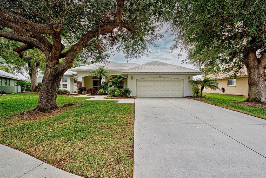 A single-story house with a beige exterior, a two-car garage, and large shade trees — 339 MEADOW BEAUTY COURT, VENICE, FL