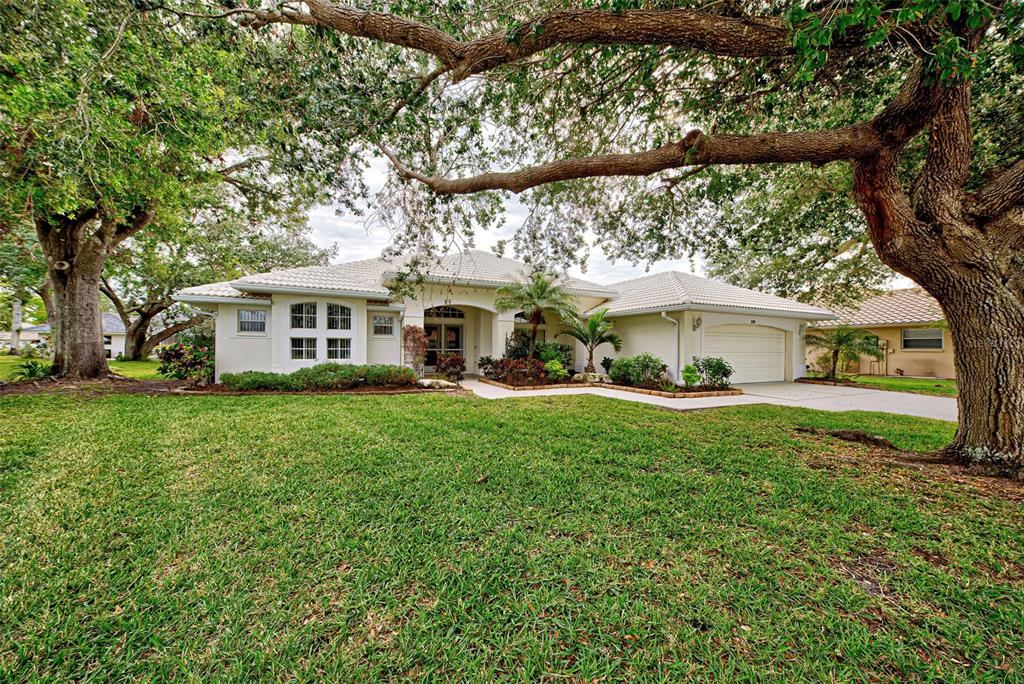 A single-story house with a light-colored exterior, tiled roof, and large oak trees in front — 339 MEADOW BEAUTY COURT, VENICE, FL