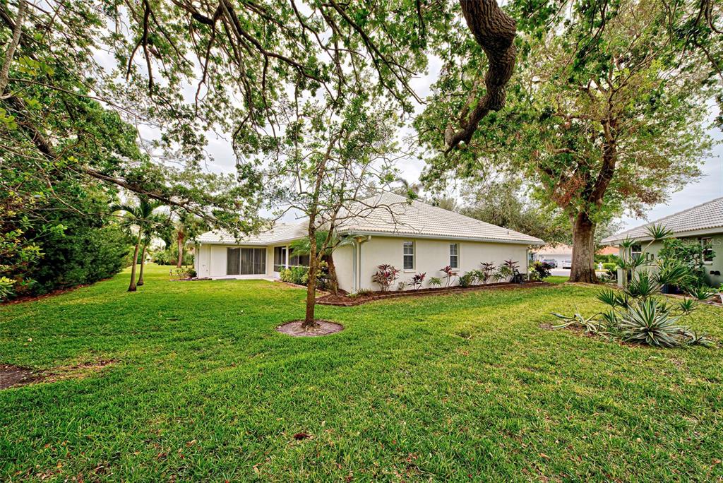 A light-colored house with a tiled roof sits on a grassy lawn under large trees — 339 MEADOW BEAUTY COURT, VENICE, FL