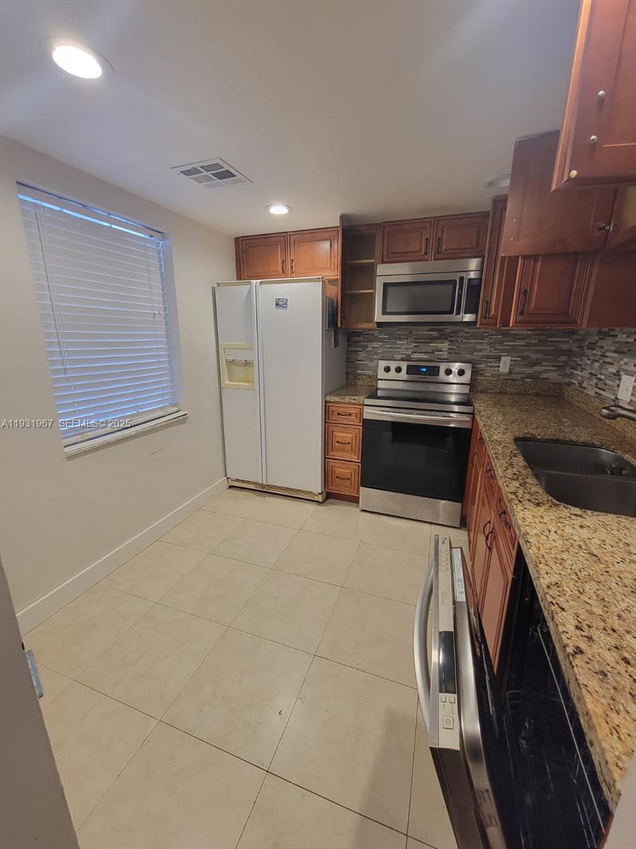 A kitchen features wood cabinets, granite countertops, stainless steel appliances, and light-colored tile flooring — 4321 NW 9th Ave # 102, Deerfield Beach FL 33064, DEERFIELD BEACH, FL