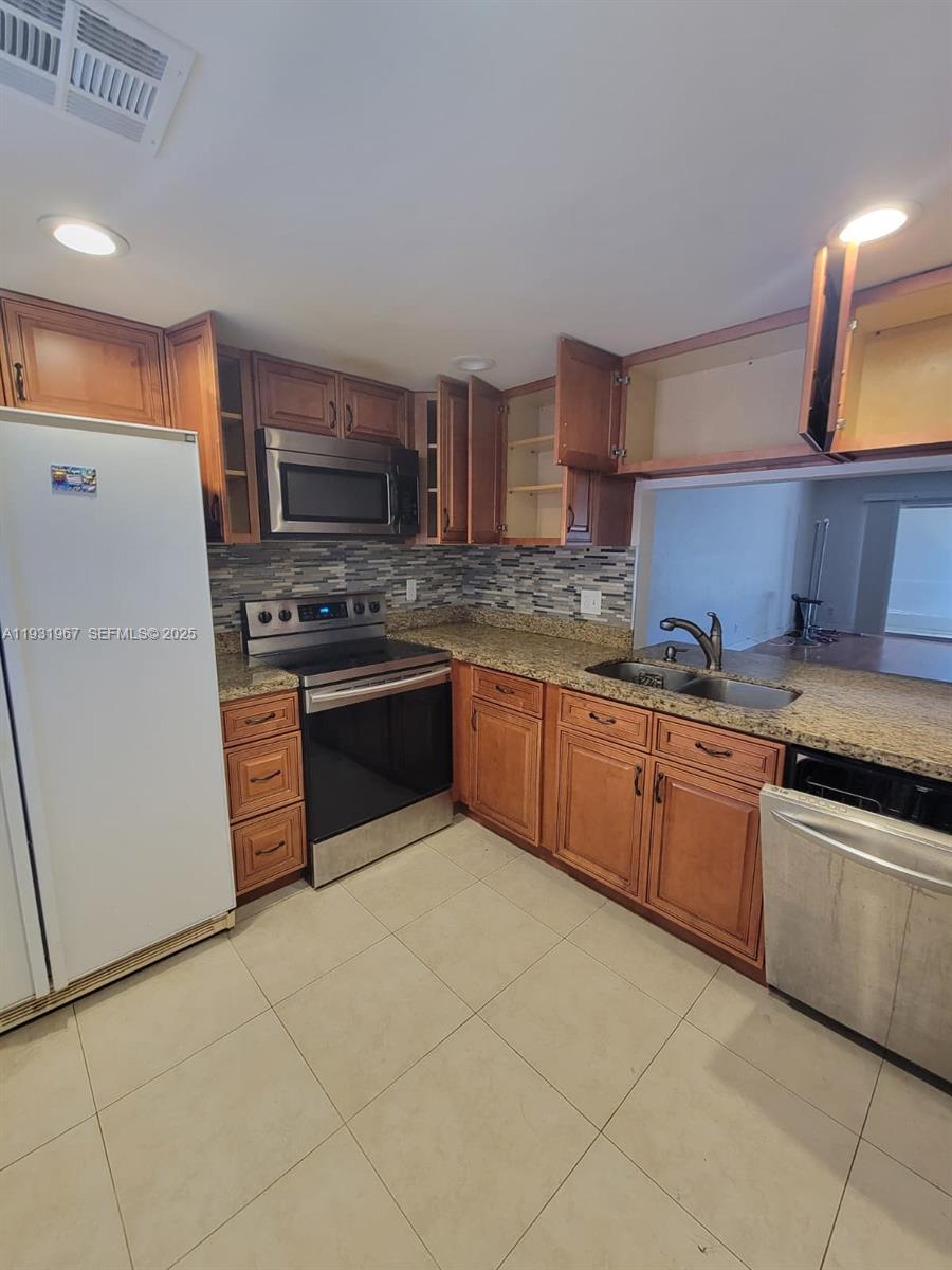 A kitchen features wood cabinets, granite countertops, stainless steel appliances, and a tile floor — 4321 NW 9th Ave # 102, Deerfield Beach FL 33064, DEERFIELD BEACH, FL