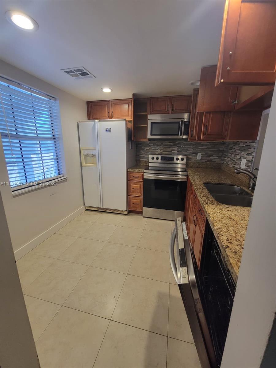 A kitchen with wood cabinets, granite countertops, stainless steel appliances, and light-colored tile flooring — 4321 NW 9th Ave # 102, Deerfield Beach FL 33064, DEERFIELD BEACH, FL