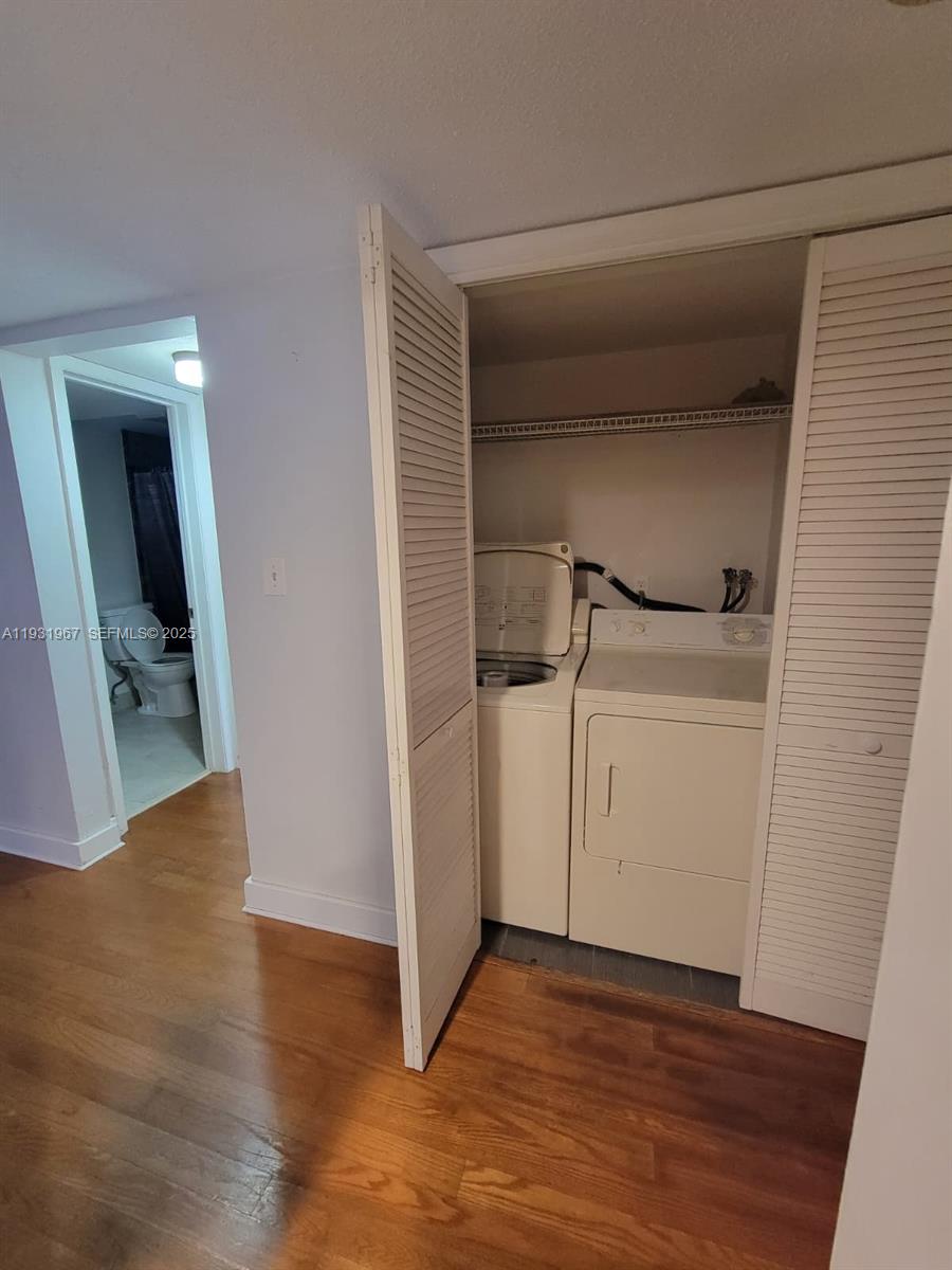 A laundry closet with a washer and dryer sits beside a doorway leading to a bathroom — 4321 NW 9th Ave # 102, Deerfield Beach FL 33064, DEERFIELD BEACH, FL