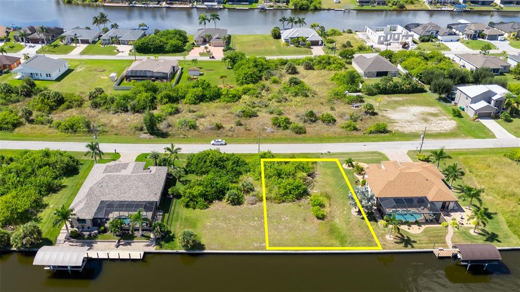 An aerial view shows a vacant waterfront lot outlined in yellow between two existing houses — 8300 TECUMSEH CIRCLE, PORT CHARLOTTE, FL