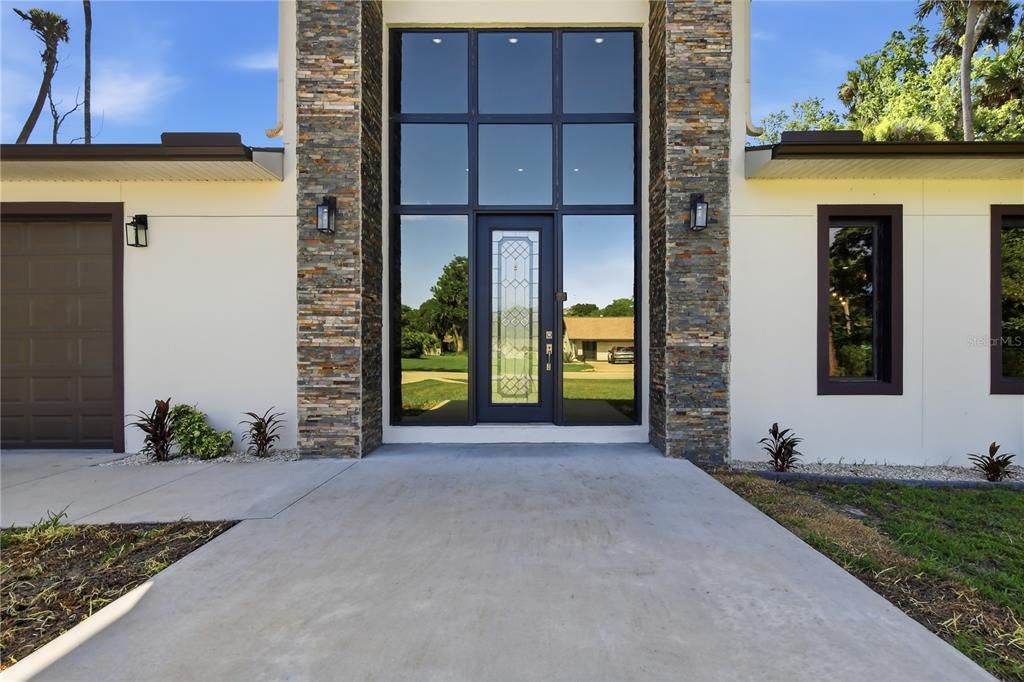 A modern home exterior features a stone-clad entryway with a tall glass door and windows — 118 BLARE DRIVE, PALM COAST, FL