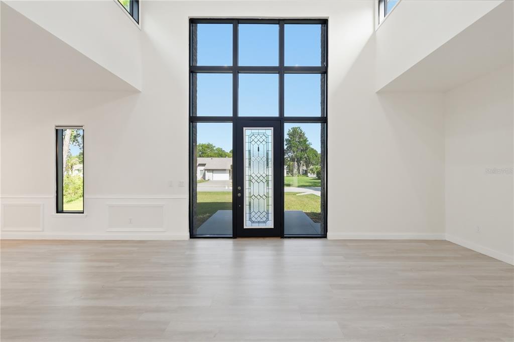 A bright, minimalist entryway features light wood flooring, white walls, and a large glass-paneled door — 118 BLARE DRIVE, PALM COAST, FL