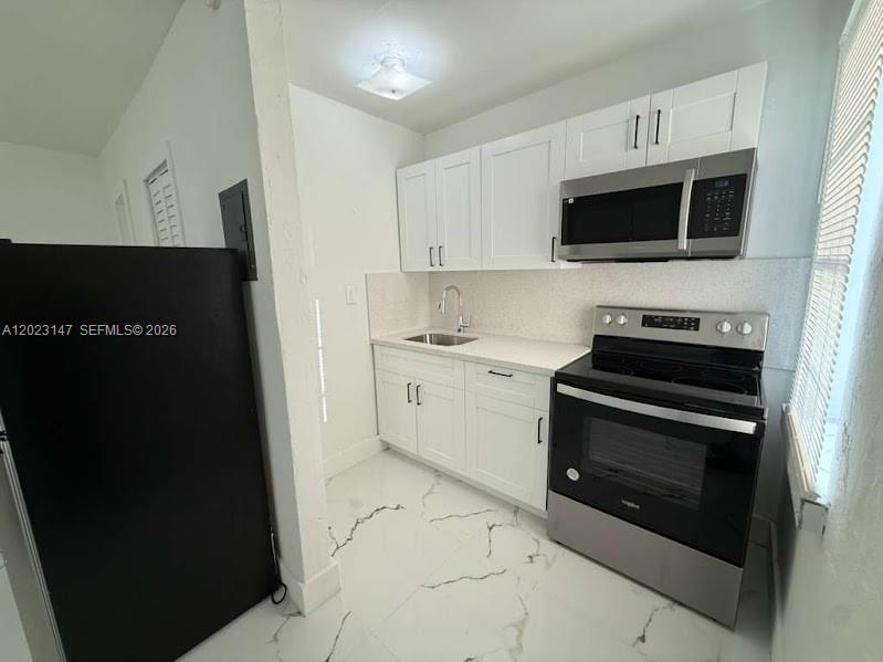 A small kitchen features white cabinets, stainless steel appliances, and white marble-patterned tile flooring — 2773 NW 57th St, Miami FL 33142, MIAMI, FL