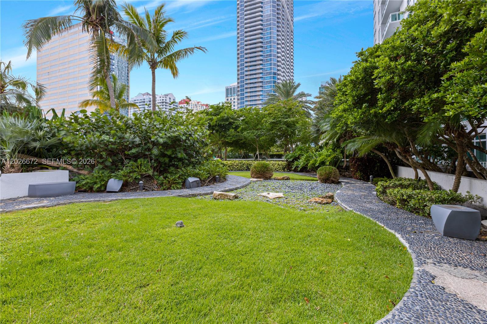 A landscaped garden features a grassy lawn, stone pathways, and palm trees near tall buildings — 951 Brickell Ave # 1801, Miami FL 33131, MIAMI, FL