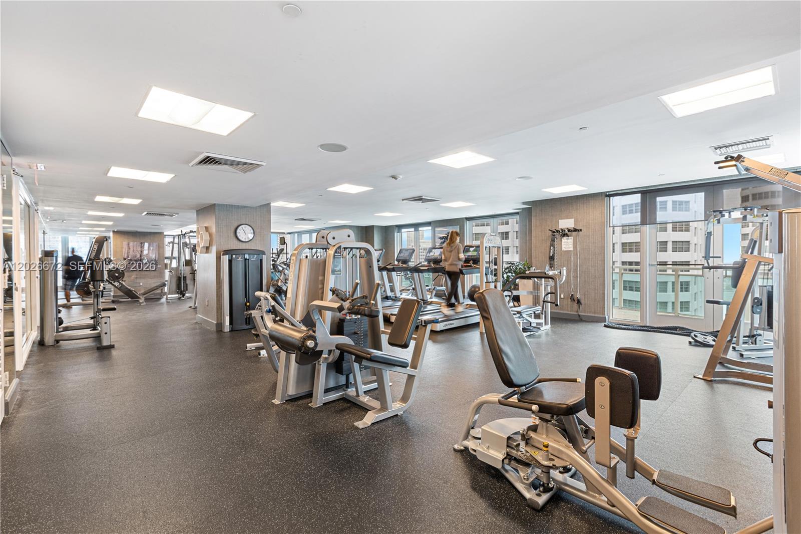 A gym features various weight machines, treadmills, and large windows overlooking a city skyline — 951 Brickell Ave # 1801, Miami FL 33131, MIAMI, FL