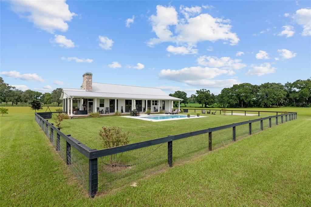A white farmhouse with a metal roof, brick chimney, and pool sits in a fenced yard — 2152 NE 120TH PLACE, ANTHONY, FL