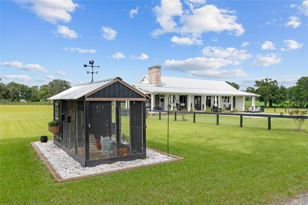 A black chicken coop sits on a gravel pad in front of a white farmhouse — 2152 NE 120TH PLACE, ANTHONY, FL
