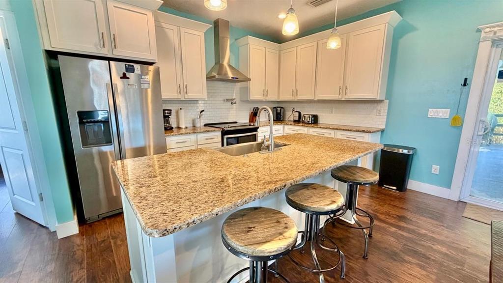 A kitchen features white cabinets, granite countertops, a central island with stools, and stainless appliances — 8 MOODY DRIVE, PALM COAST, FL