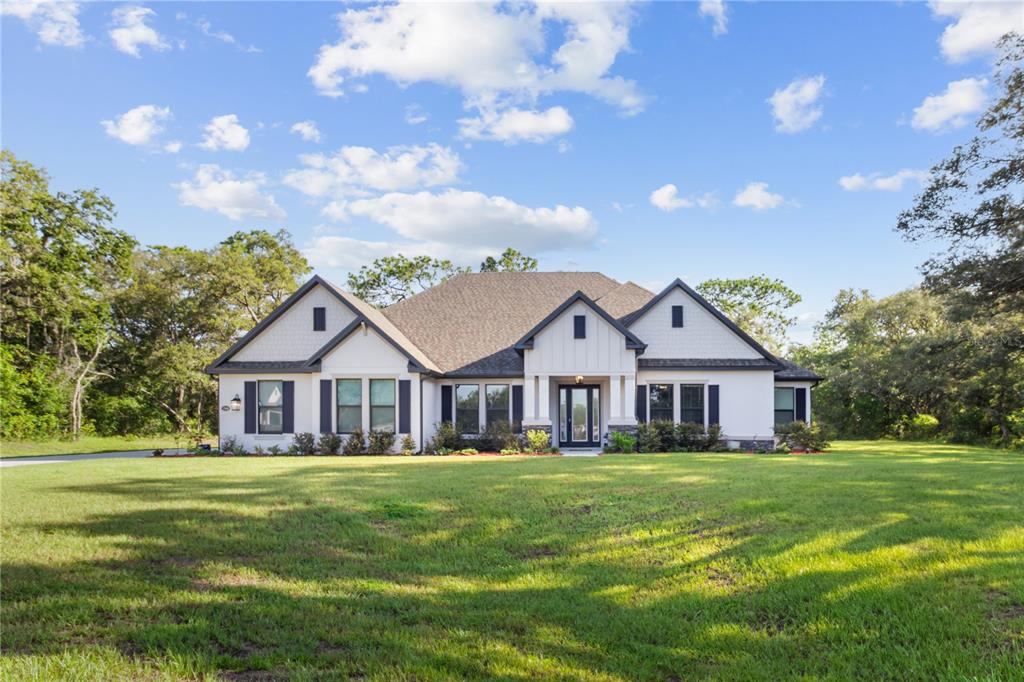 A single-story white house with dark shutters and a gabled roof sits on a lawn — 17000 NOKOTA AVENUE, HUDSON, FL
