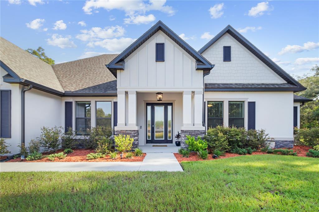 A single-story house with white siding, stone accents, a covered entryway, and a dark roof — 17000 NOKOTA AVENUE, HUDSON, FL