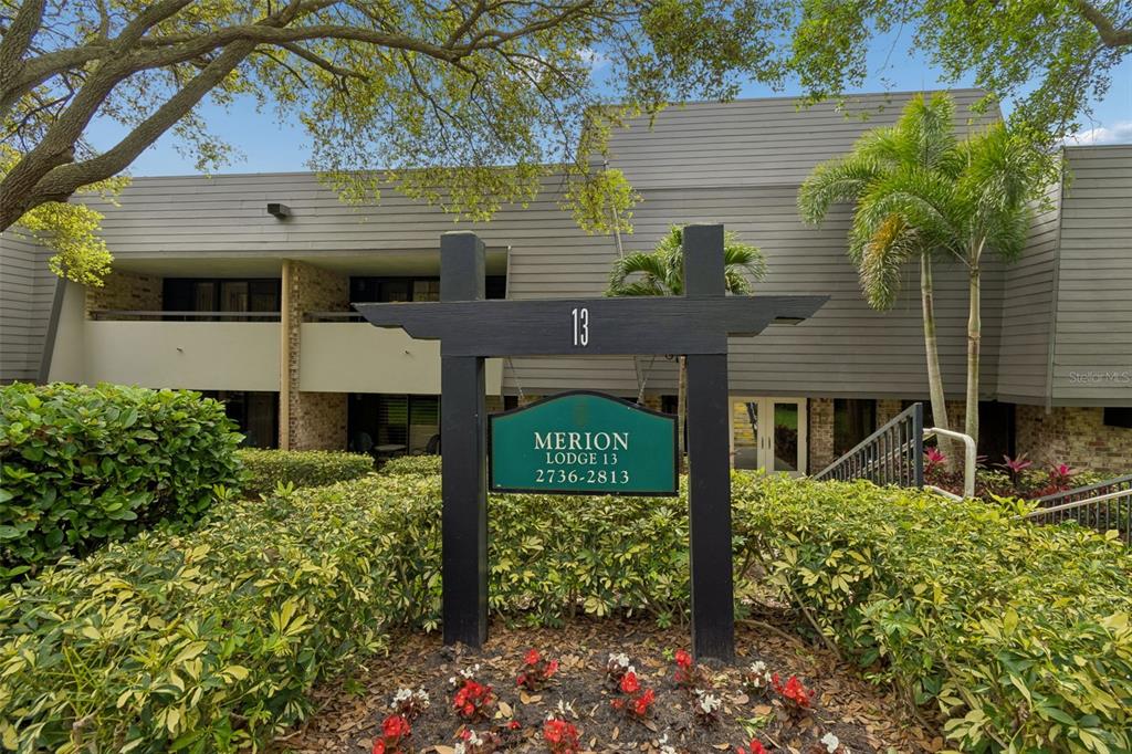 A sign for Merion Lodge 13 stands in front of a two-story building with landscaping — 36750 US HIGHWAY 19 N UNIT 13118, PALM HARBOR, FL