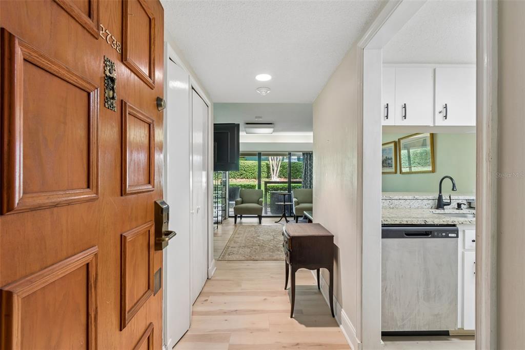 A view from an open wooden front door into a hallway with light wood flooring — 36750 US HIGHWAY 19 N UNIT 13118, PALM HARBOR, FL